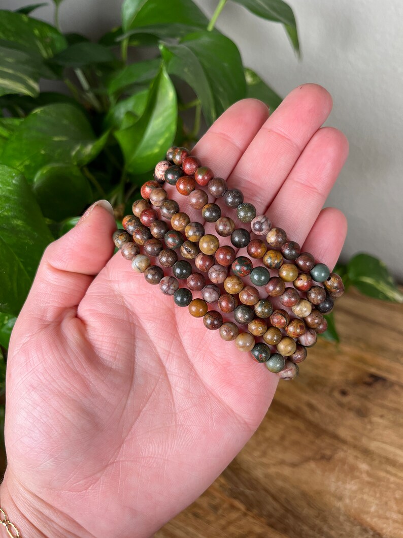 May include: A stack of six bracelets made with brown, green, and red jasper beads.
