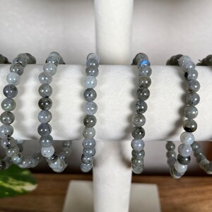 May include: Five grey labradorite beaded bracelets on a white display stand. The bracelets are made of round beads and are all the same size.