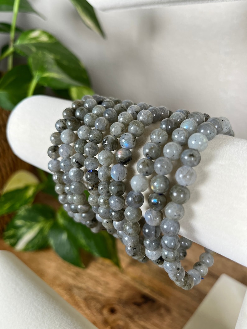 May include: A stack of grey labradorite gemstone bracelets. Each bracelet is made of round beads and has a subtle iridescent sheen.