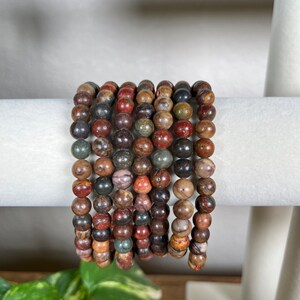 May include: A stack of bracelets made with multi-colored, round, gemstone beads. The beads are a mix of brown, red, green, and black.