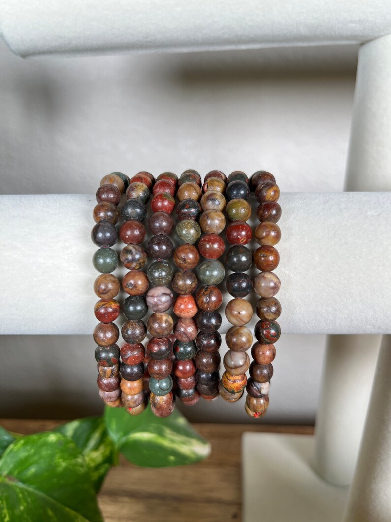 May include: A stack of bracelets made with multi-colored, round, gemstone beads. The beads are a mix of brown, red, green, and black.