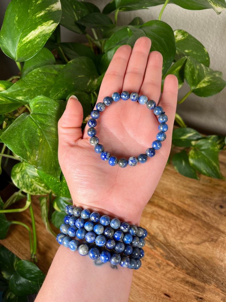May include: A stack of blue lapis lazuli beaded bracelets. The bracelets are made with round beads and have a dark blue color with flecks of gold.