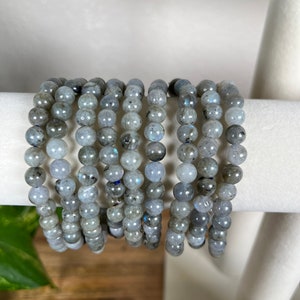May include: A stack of grey labradorite gemstone bracelets. Each bracelet is made of round beads and has a subtle iridescent sheen.