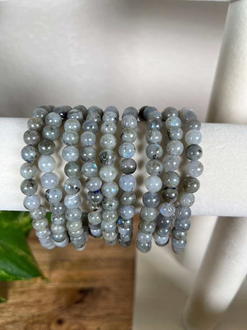 May include: A stack of grey labradorite gemstone bracelets. Each bracelet is made of round beads and has a subtle iridescent sheen.