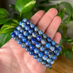 May include: A stack of blue and white lapis lazuli gemstone bracelets. The bracelets are made with round beads and are stacked on top of each other.