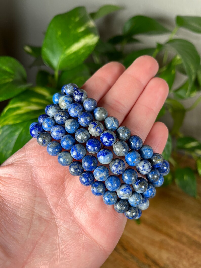 May include: A stack of blue and white lapis lazuli gemstone bracelets. The bracelets are made with round beads and are stacked on top of each other.