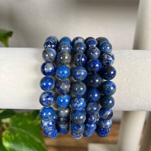 May include: A stack of five blue lapis lazuli beaded bracelets. The beads are round and have a speckled pattern.