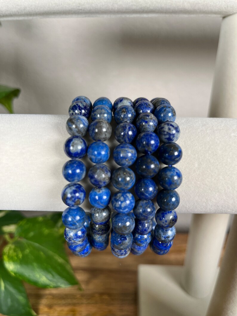 May include: A stack of five blue lapis lazuli beaded bracelets. The beads are round and have a speckled pattern.