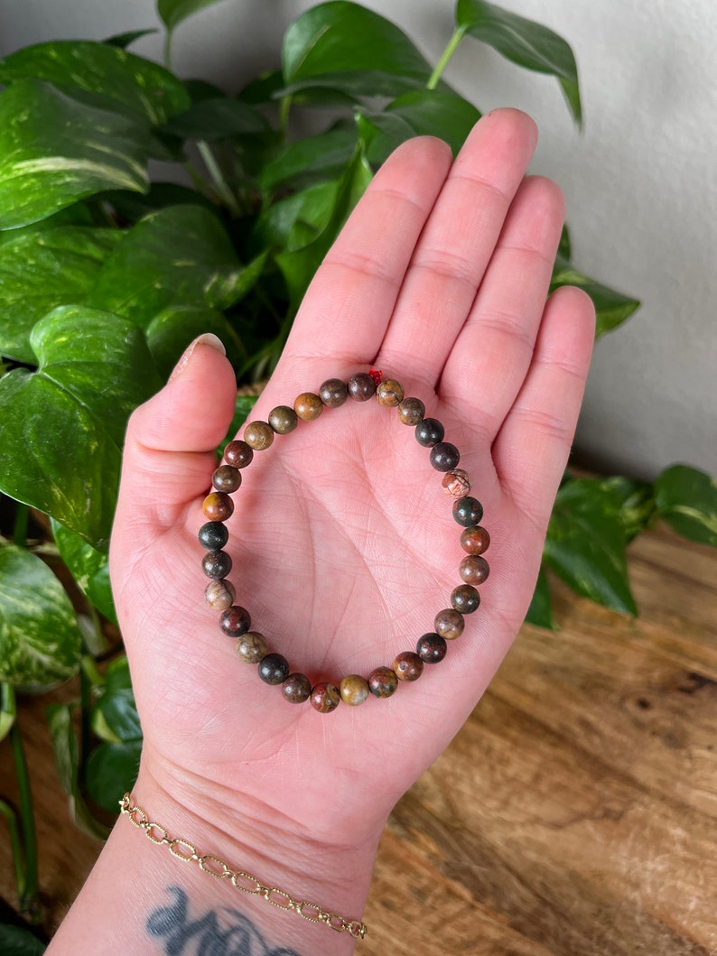 May include: A brown, green, and red beaded bracelet with a red string closure.