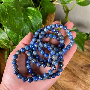 May include: A set of three blue and white lapis lazuli beaded bracelets. The bracelets are made of round beads and are stacked on top of each other.