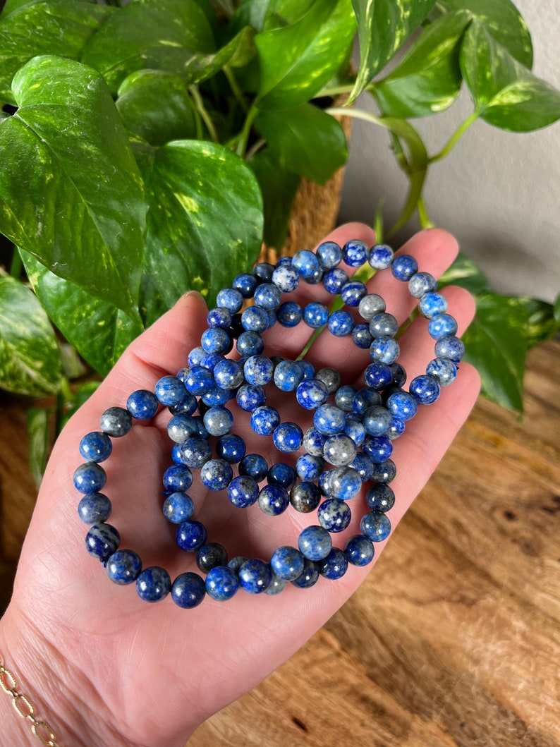 May include: A set of three blue and white lapis lazuli beaded bracelets. The bracelets are made of round beads and are stacked on top of each other.