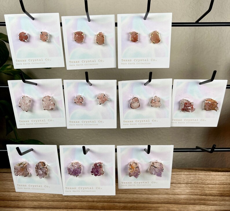 Pu&ograve; includere: Dieci paia di orecchini di cristallo su schede con il testo "Texas Crystal Co. Rare Earth Collection". Gli orecchini sono realizzati con vari cristalli, tra cui rosa, viola e arancio.