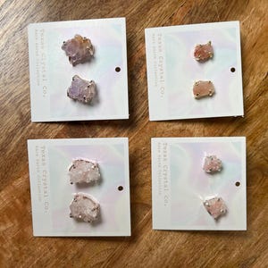 Pu&ograve; includere: Quattro paia di orecchini con grappoli di cristalli grezzi in varie tonalit&agrave; di rosa e viola. Ogni paio &egrave; esposto su una carta bianca con il testo "Texas Crystal Co. Rare Earth Collection".