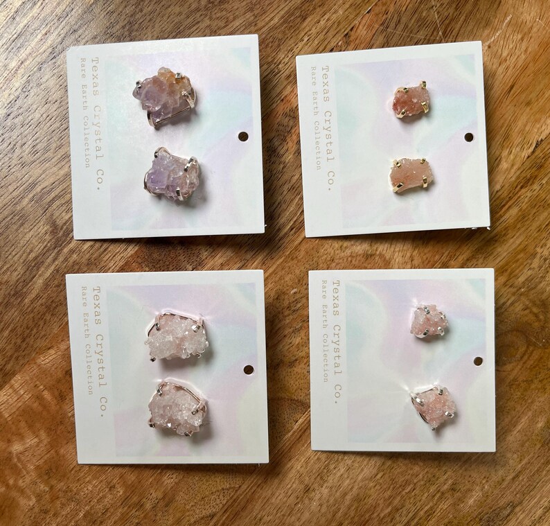 Pu&ograve; includere: Quattro paia di orecchini con grappoli di cristalli grezzi in varie tonalit&agrave; di rosa e viola. Ogni paio &egrave; esposto su una carta bianca con il testo "Texas Crystal Co. Rare Earth Collection".