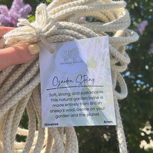 May include: A close-up of a roll of natural, cream-coloured garden twine made from British sheep's wool. The twine is 6mm thick and 10 metres long. The label reads "Garden String" and "Sustainable Rope Ltd."