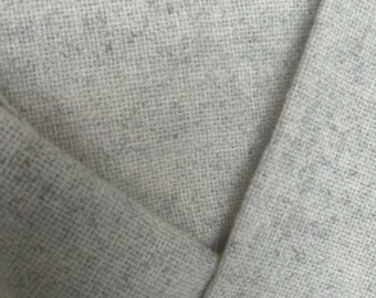 Pode incluir: Close-up de tecido cinza claro com textura tecida. O tecido está dobrado, revelando o interior e as bordas. O material parece macio e tem um padrão sutil e salpicado.