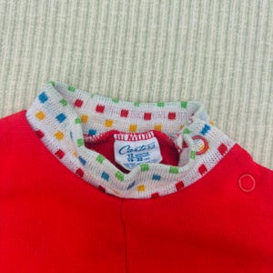 Puede incluir: Mono rojo de manga larga con cuello de patr&oacute;n blanco y colorido. El mono tiene una etiqueta de Carter's que dice "12 meses 18-22 in."