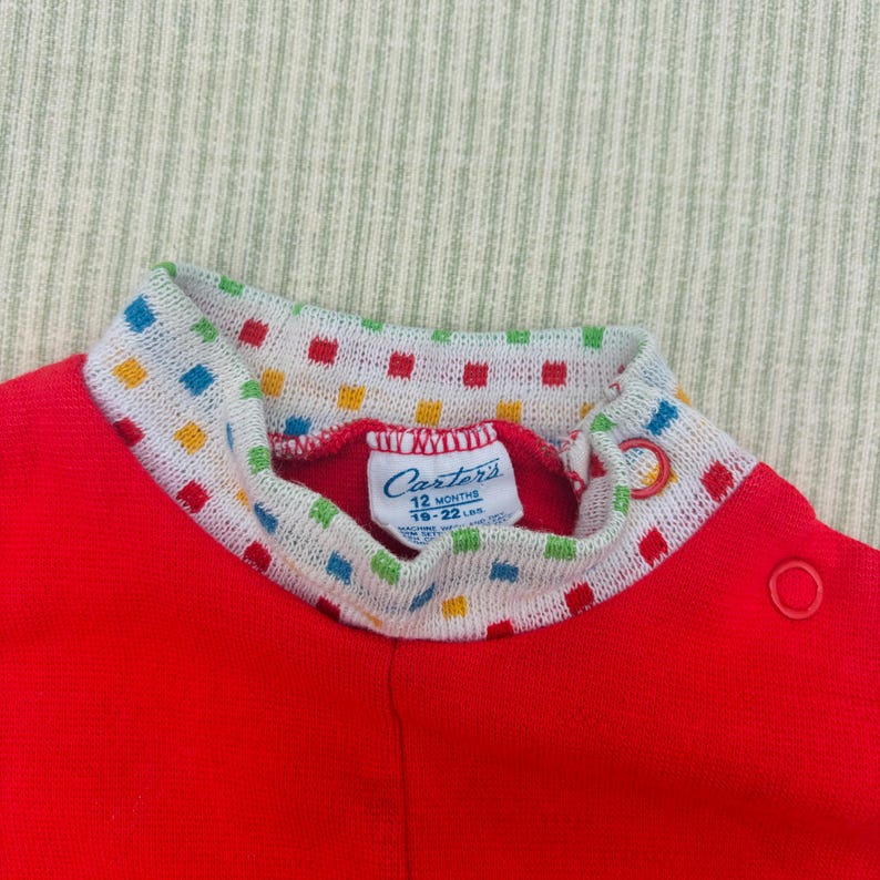 Puede incluir: Mono rojo de manga larga con cuello de patr&oacute;n blanco y colorido. El mono tiene una etiqueta de Carter's que dice "12 meses 18-22 in."