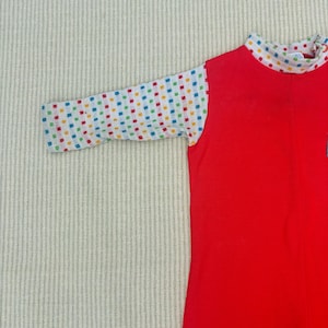 Puede incluir: Camiseta roja de manga larga con un patr&oacute;n de cuadros blancos y coloridos en las mangas.