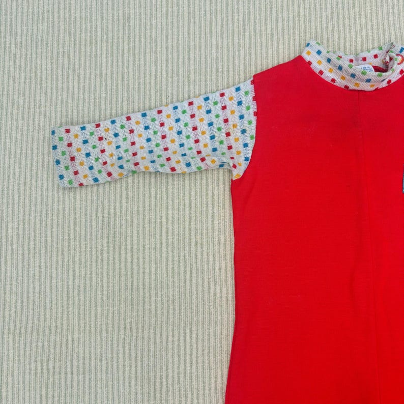 Puede incluir: Camiseta roja de manga larga con un patr&oacute;n de cuadros blancos y coloridos en las mangas.