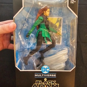 May include: A boxed action figure of Cyclone from the DC Multiverse Black Adam series. The figure is in a dynamic pose, wearing a black and green costume with red hair. The packaging is black with the DC Multiverse and Black Adam logos.