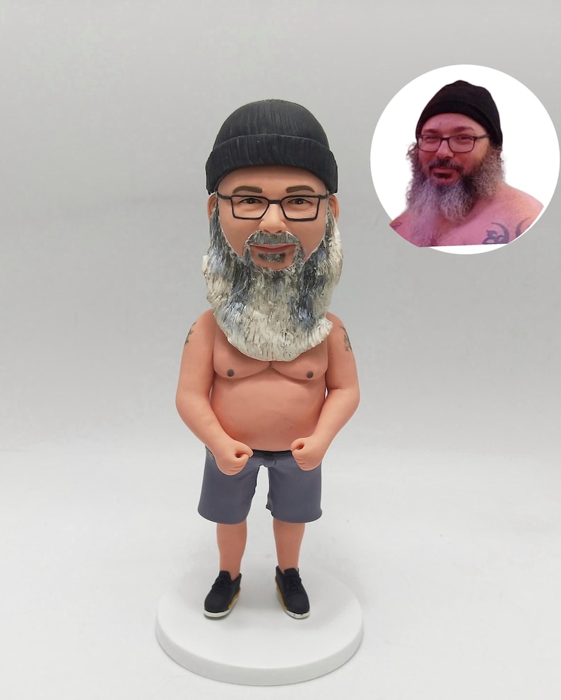 May include: A custom figurine of a man wearing a black beanie and glasses, with a long, grey beard. He is dressed in grey shorts and black trainers. A smaller image of the man is in the background. The figurine stands on a white circular base.