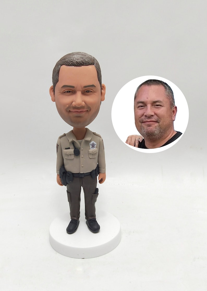May include: A custom-made figurine of a person wearing a tan uniform with a badge and a black belt. The figurine has a realistic face and is standing on a white base.