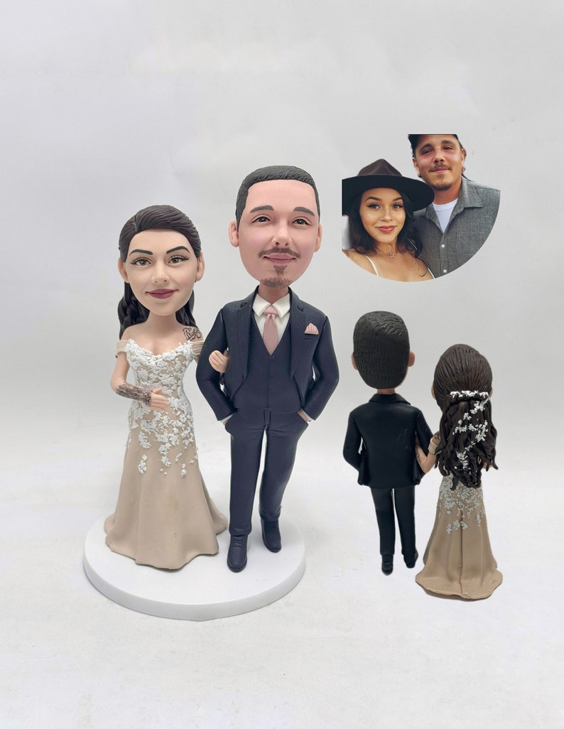 May include: A wedding cake topper featuring a bride and groom in a traditional wedding attire. The bride is wearing a beige dress with white lace details and the groom is wearing a black suit with a pink tie. The couple is also shown from the back, with the bride wearing a beige dress with white lace details and the groom wearing a black suit.