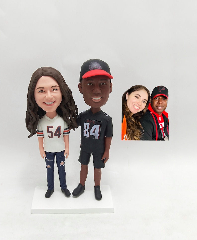 May include: A custom-made figurine set of a couple wearing sports jerseys. The woman is wearing a white jersey with the number 54 and blue jeans. The man is wearing a black jersey with the number 84 and black shorts. The figurines are standing on a white base.