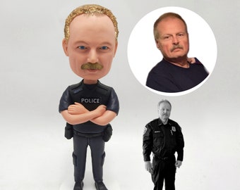 May include: A custom bobblehead figurine of a person wearing a police uniform with the word "POLICE" on the chest. The figurine is standing with arms crossed and has a mustache. The bobblehead is on a white base.