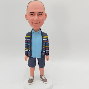 Könnte beinhalten: Eine benutzerdefinierte Figur einer Person mit Glatze, die ein blau-weiß gestreiftes Hemd, eine blau-mehrfarbig gestreifte Jacke, blaue Shorts und braune Turnschuhe trägt.