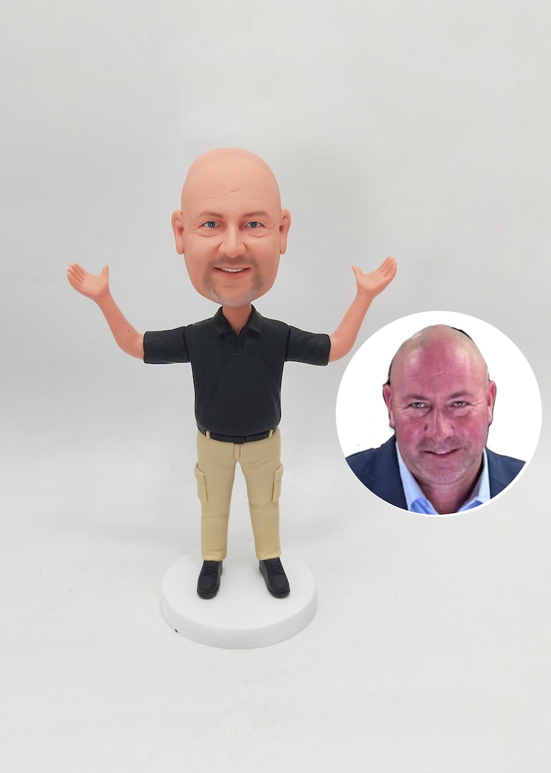 May include: A custom-made figurine of a person with a bald head, wearing a black polo shirt, khaki pants, and black shoes. The figurine is standing with arms outstretched. A close-up photo of the person's face is shown in a circle.