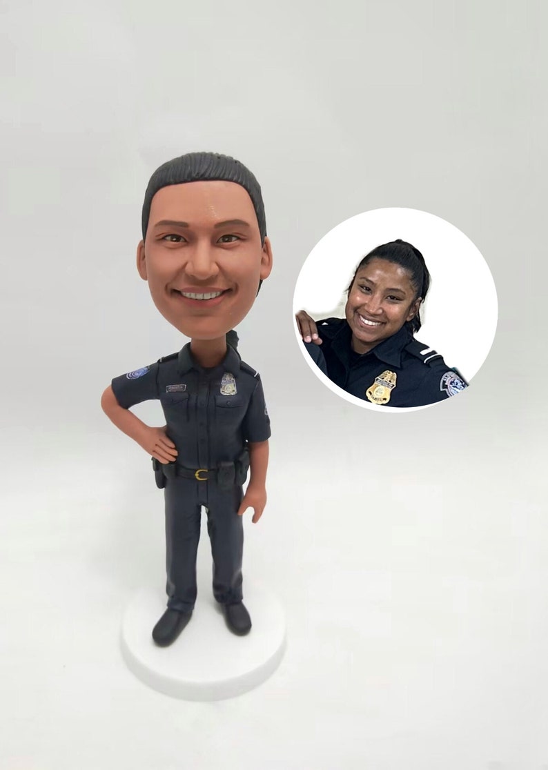 May include: A bobblehead figurine of a smiling police officer in a dark blue uniform, standing on a white base. A smaller image of a smiling woman in a police uniform is in the background.