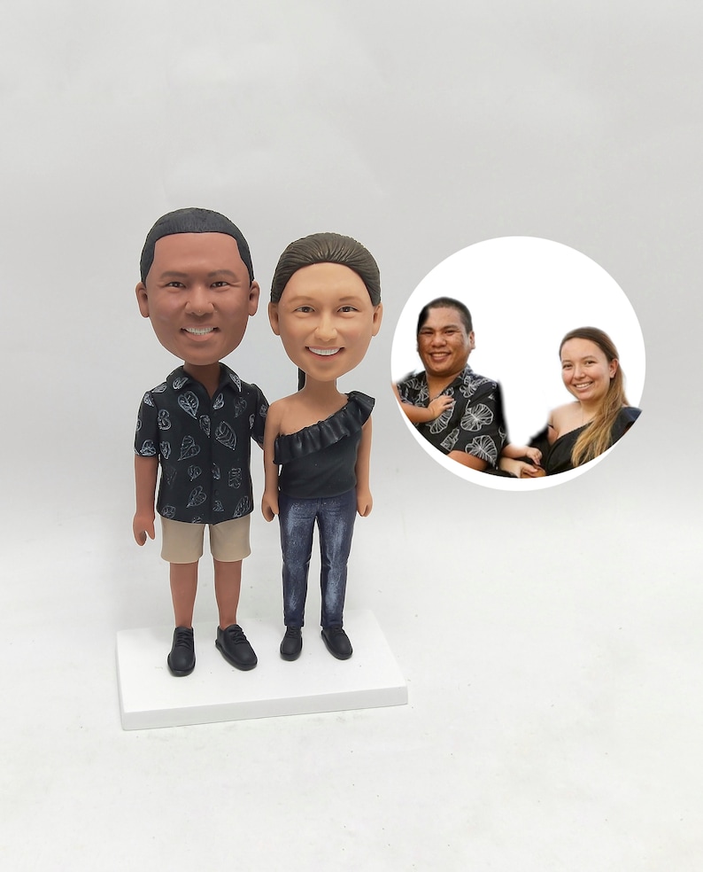 May include: A custom-made figurine set of a couple, with the man wearing a black and white patterned shirt and khaki shorts, and the woman wearing a black top and blue jeans. The figurines are standing on a white base.
