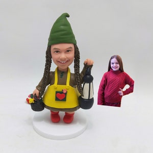 May include: A custom-made gnome figurine with a green hat, brown hair, and a yellow apron with a red heart. The gnome is holding a lantern and a basket of flowers.