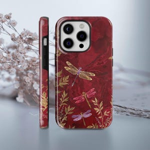 Könnte beinhalten: Eine rote iPhone-Hülle mit Marmormuster und goldenen Akzenten. Die Hülle zeigt ein Muster aus zarten Libellen mit goldenen und violetten Flügeln.