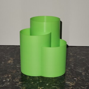 May include: A bright green three-sectioned desktop organizer made of plastic. The organizer has three separate compartments for holding pens, pencils, or other office supplies.