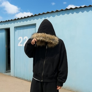 Peut inclure: Un sweat à capuche noir zippé avec une capuche bordée de fausse fourrure marron et beige. Le vêtement comprend une fermeture éclair frontale intégrale, des manches longues avec des poignets côtelés et une poche kangourou sur le devant.