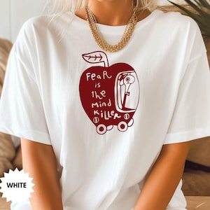 May include: White t-shirt with a red apple graphic. The apple has a face and the text "Fear is the Mind Killer" inside.