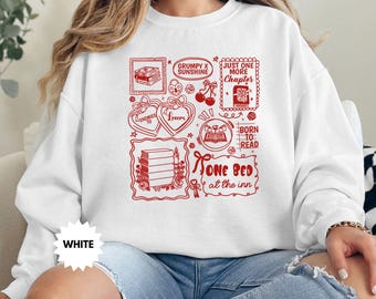 Op de afbeelding: Witte sweatshirt met rode grafische illustraties en tekst. Het ontwerp bevat boekenstapels, harten, kersen en de zinnen "Grumpy x Sunshine", "Just One More Chapter", "Born to Read" en "One Bed at the Inn".