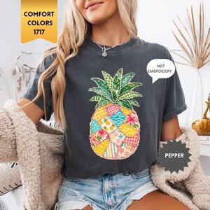 May include: Charcoal grey t-shirt with a patchwork pineapple design. The pineapple is made up of various colorful fabric patterns. The text "NOT EMBROIDERY" is displayed. The shirt is labeled "COMFORT COLORS 1717" and "PEPPER".