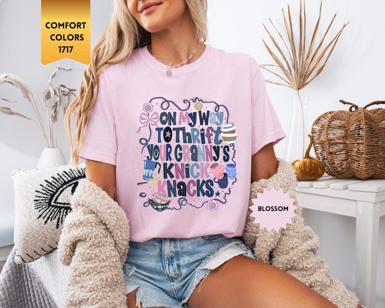 Może przedstawiać: Jasnor&oacute;żowa koszulka z napisem "ON MY WAY TO THRIFT YOUR GRANNY'S KNICK KNACKS" w fantazyjnym wzorze. Koszulka jest oznaczona jako "Blossom" i "Comfort Colors 1717".