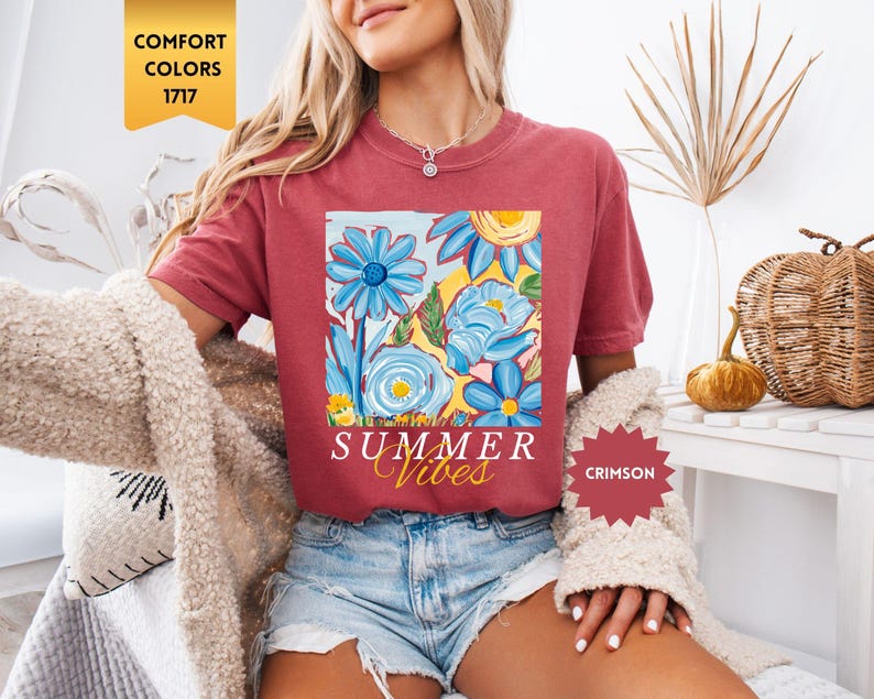 Peut inclure: Un t-shirt rouge avec un motif floral et le texte "Summer Vibes" en blanc. Le t-shirt est port&eacute; par une personne aux cheveux blonds. Le texte "Crimson" est visible dans un cercle rouge.