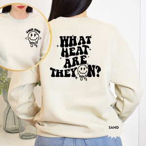 May include: A cream coloured sweatshirt with a black graphic on the back that says "WHAT HEAT ARE THEY ON?" with a dripping smiley face. The front of the sweatshirt has a black graphic of a dripping smiley face with the text "SWIM MOM".