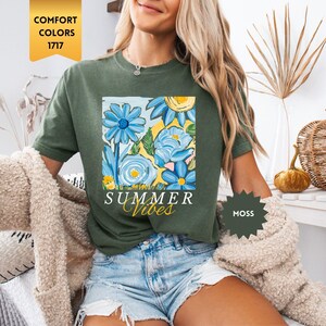Peut inclure: Une femme portant un t-shirt vert avec un motif floral et le texte "Summer Vibes". Elle porte &eacute;galement un short en jean et un cardigan beige.