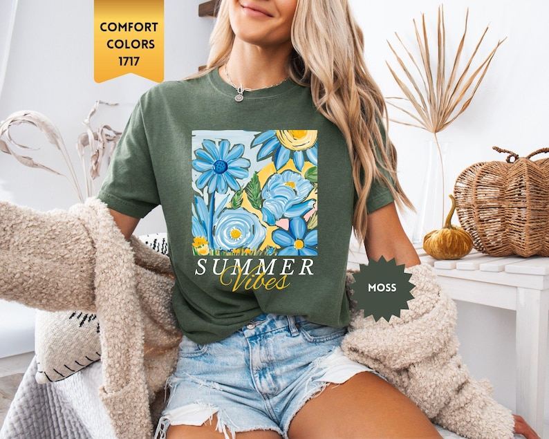 Peut inclure: Une femme portant un t-shirt vert avec un motif floral et le texte "Summer Vibes". Elle porte &eacute;galement un short en jean et un cardigan beige.