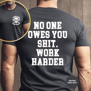 Op de afbeelding: Donkergrijze heather t-shirt met de witte tekst "NO ONE OWES YOU SHIT. WORK HARDER" op de rug. De voorkant toont een schedel- en moersleutelafbeelding met de tekst "NOBODY CARES WORK HARDER".