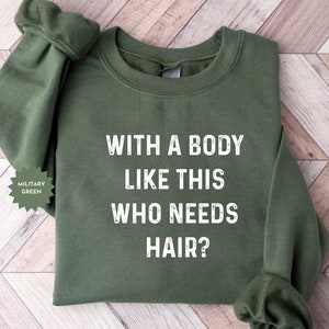 May include: A military green sweatshirt with the text "WITH A BODY LIKE THIS WHO NEEDS HAIR?" printed in white.