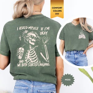 May include: Moss green t-shirt with a skeleton graphic wearing sunglasses, holding a drink, and the text "I asked myself if I'm okay, and we both started laughing." The shirt also has a small graphic on the front. Comfort Colors 1717.