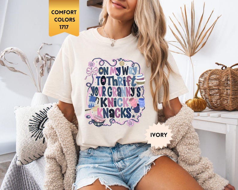 Może przedstawiać: Kremowa koszulka z napisem "ON MY WAY TO THRIFT YOUR GRANNY'S KNICK KNACKS" w kolorowym, fantazyjnym wzorze. Koszulka jest w stylu Comfort Colors 1717.